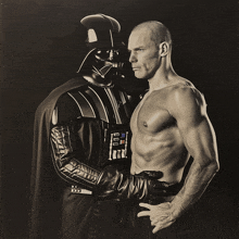 a shirtless man stands next to a darth vader