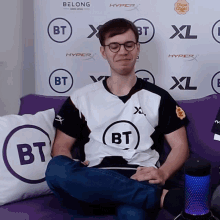 a man sits on a couch in front of a wall that says bt