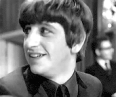 a black and white photo of a young man smiling in a suit and tie .