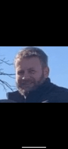 a man with a beard is smiling for the camera while wearing a black jacket .