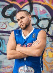 a man in a blue basketball jersey is standing in front of a graffiti covered wall .