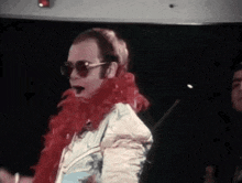 elton john is wearing sunglasses and a red boa around his neck while dancing on stage .