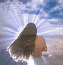 a woman with long hair stands on a beach with the sun shining through the clouds