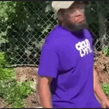 a man wearing a purple shirt and a white hat is walking in front of a chain link fence .