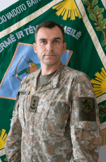 a man in a military uniform stands in front of a green banner that says " erme ir te "