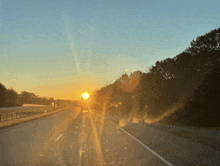 the sun is setting over a highway with trees on both sides