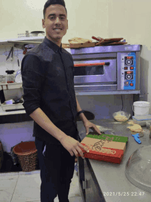 a man holds a pizza box in front of a pizza oven