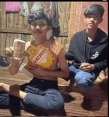 a man and a woman are sitting on the floor eating chips and drinking beer .