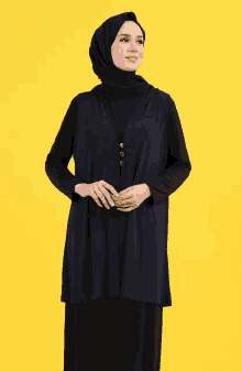 a woman wearing a black hijab and a blue vest is standing on a yellow background