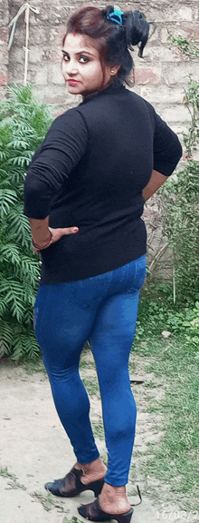 a woman in a black sweater and blue jeans is standing with her hands on her hips