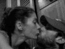 a black and white photo of a man and a woman kissing .