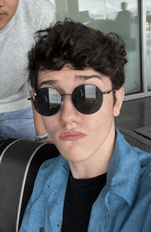 a young man wearing sunglasses and a blue shirt makes a funny face