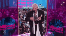 a man in a tuxedo is holding a trophy in front of a crowd at a billboard music awards show .