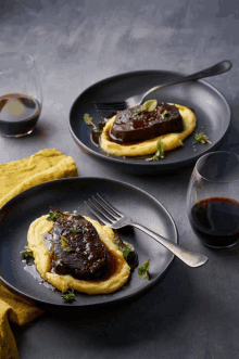 two plates of food on a table with a glass of wine in the background