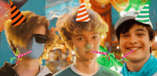 three young men wearing party hats are standing next to each other and blowing party horns .