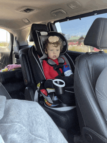 a toddler is sitting in a car seat with a cup holder in the back seat