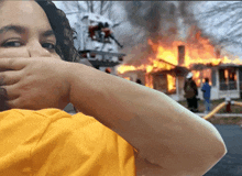 a woman covering her mouth in front of a house on fire