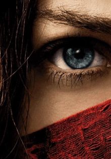 a close up of a woman 's blue eye with a red cloth covering her face