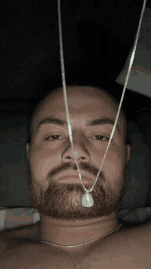 a man with a beard is laying down with two necklaces hanging from his neck