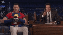 a man in a superhero costume is sitting next to a man in a suit and tie .