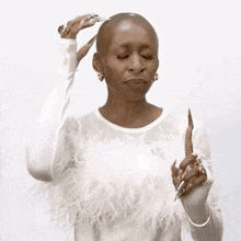 a woman with a shaved head is wearing a white feathered top and holding a pen .