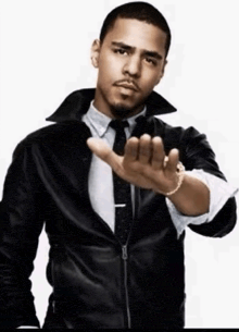 a man wearing a leather jacket and tie is making a stop gesture