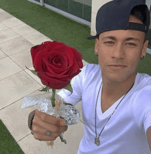 a man wearing a hat and a white shirt holds a red rose