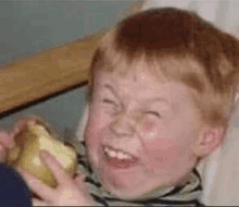 a little boy is making a funny face while holding a piece of apple .