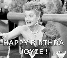 a black and white photo of a woman sitting at a table with a martini glass and saying `` happy birthday joyce ! ''