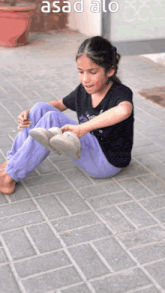 a little girl is sitting on the sidewalk with the word asad written on the bottom