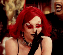 a woman with red hair and black gloves holds her hand to her face