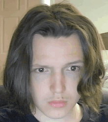 a young man with long hair is taking a selfie with his eyes closed .