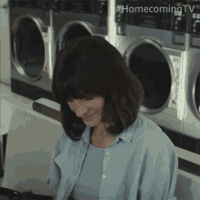 a woman sits in front of a row of washing machines in a laundromat with homecoming tv written on the bottom