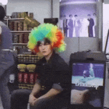 a man wearing a rainbow colored wig is sitting in front of a television .