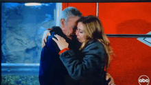 a man and a woman are hugging in front of a red abc sign