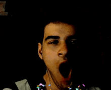 a man with a beard is yawning in a dark room with confetti falling around his neck