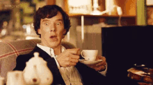 a man in a suit is sitting on a couch holding a cup of tea .