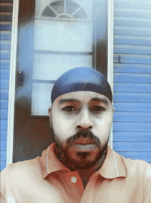 a man with a beard wearing a blue headband stands in front of a blue building