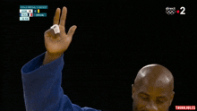 a man in a blue kimono holds up his index finger in front of a screen that says gold medal contest