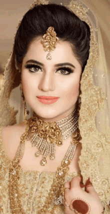 a bride wearing a veil and gold jewelry is looking at the camera