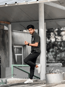 a young man in a black shirt and white shoes leans against a white pole