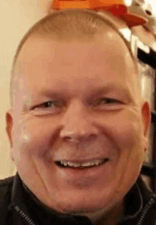 a close up of a man 's face smiling with a hat in the background .