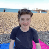 a young man is sitting on a pink and blue towel on the beach .