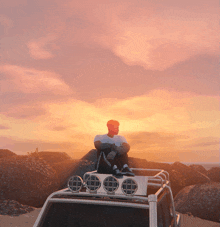 a man sits on the roof of a vehicle watching the sunset