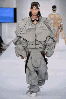 a model walks down the runway at a fashion show wearing headphones and goggles