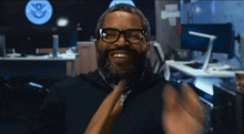 a man with glasses and a beard is smiling in front of a u.s. department of defense logo