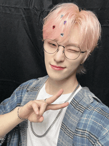 a young man wearing glasses and a plaid shirt makes a peace sign