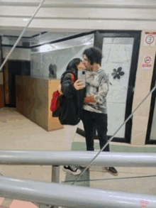 a man and a woman are kissing and taking a selfie in front of a mirror .