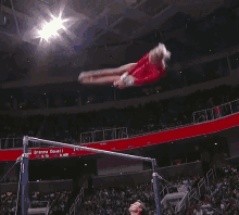 a woman in a red leotard is doing a trick on a bar with a sign that says brenna dowell in the background