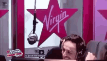 a man wearing headphones is sitting in front of a microphone in front of a virgin logo .